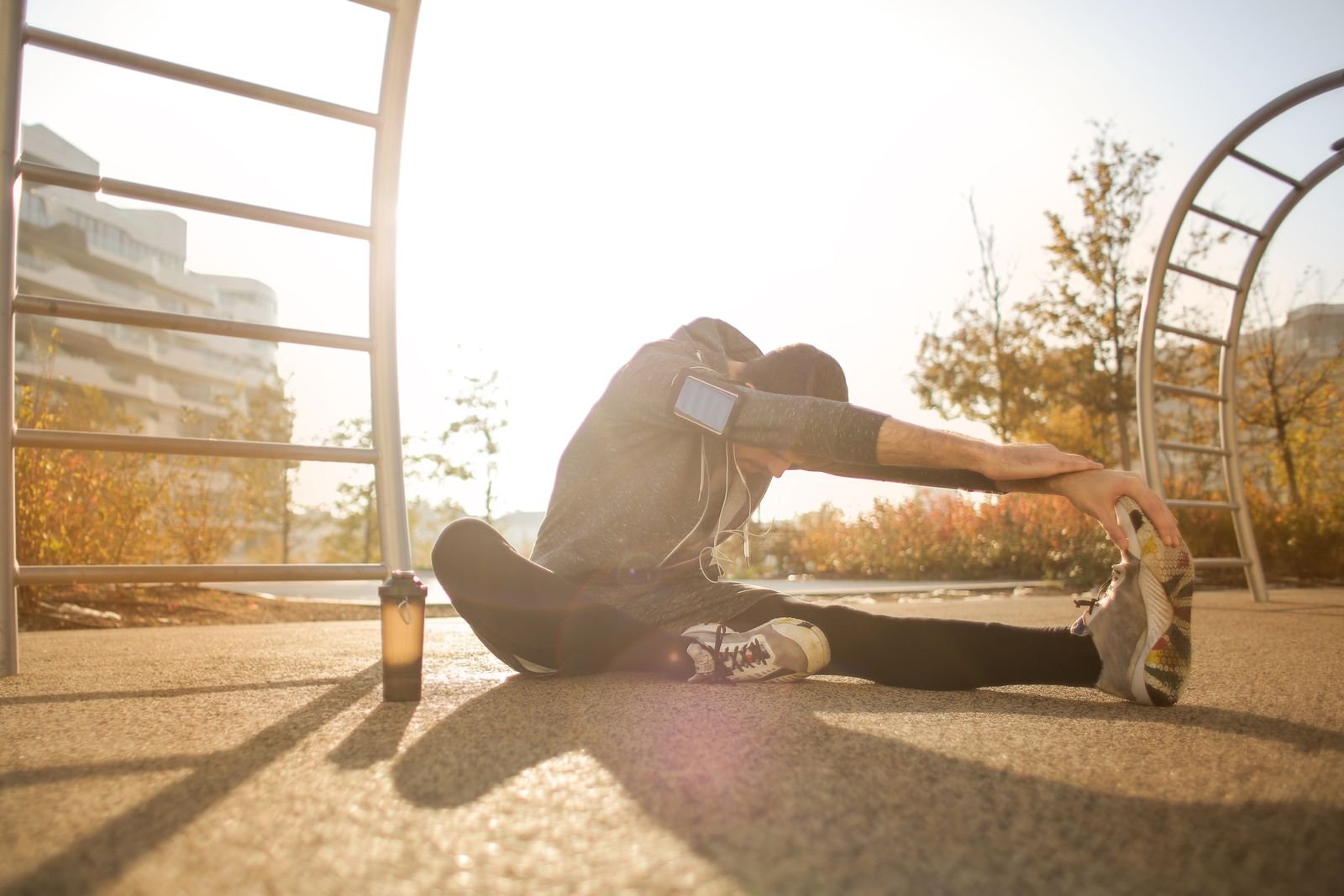 Runner in a hooded top stretching toward one shoe on an outdoor exercise ground at sunrise